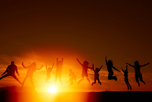 friends jumping in the sunset lights, silhouettes of people feeling carefree in nature.