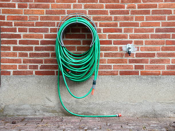 Green Garden Water Hose mounted on Red Brickwall Green Garden Water Hose Hanging on Red Brickwall. Not connected to Water Tap. garden hose stock pictures, royalty-free photos & images