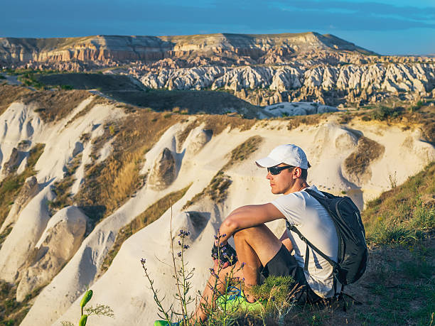 istock Young sportive man in white cap with backpack sitting on 584247334
