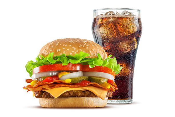 Double Cheese and Bacon Cheeseburger with Cola High resolution, digital capture of a double cheese cheeseburger with crispy bacon slices, American cheese, pickles, onions, tomatoes, lettuce, ketchup, and mustard, on a fresh sesame seed bun, set against a clean, white background sweep with a glass of cola behind it. Shot in an aspirational advertising style. bacon cheeseburger stock pictures, royalty-free photos & images