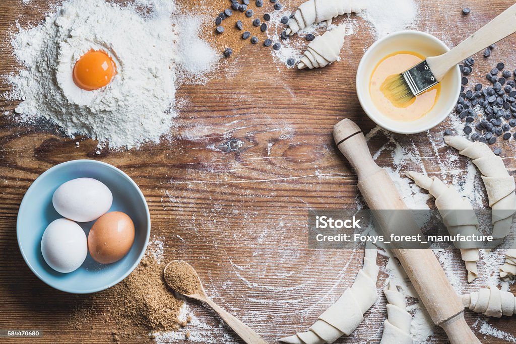 Baking ingredients for cooking croissants over wooden background, copy space Baking ingredients for cooking croissants. Eggs, brown sugar, melted butter, flour, chocolate chips over rustic wooden background. Top view, copy space Baking Stock Photo