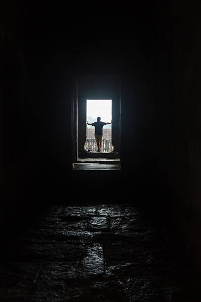 istock Male silhouette in empty interior looking in window, lit by 584472332