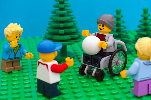 Tambov, Russian Federation - July 30, 2016 Lego boy in wheelchair playing ball with his friends in park. Studio shot.