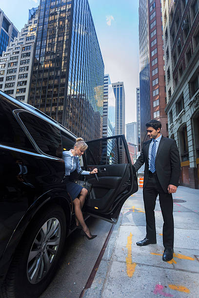Business man opening car door for woman Young business woman getting out of a luxury car while a man is holding the door open for her in downtown New York City disembarking stock pictures, royalty-free photos & images