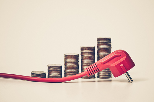 A red plug on a stack of coins arranged as a graph / Expensive electricity cost due to using too much energy consumption appliance / Effect of not using energy efficient appliances