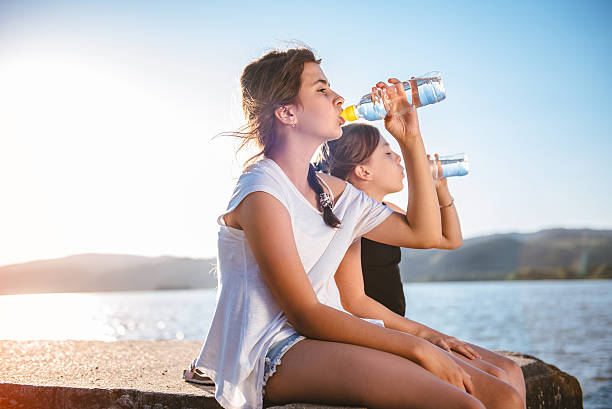 istock Two girls drinking water and sitting on dock 584489226