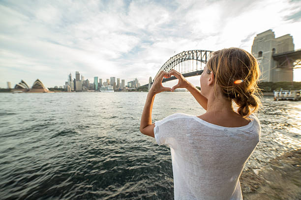 istock Young woman in Sydney harbour makes heart shape finger frame 584490110