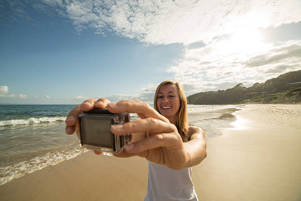 giovane donna in spiaggia scatta selfie ritratto usando action camera - australia photographing camera beach foto e immagini stock