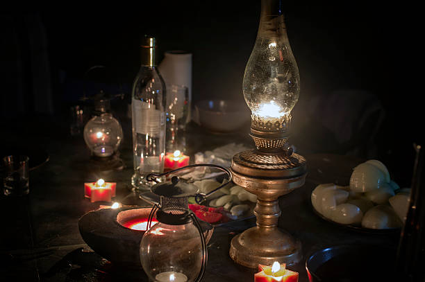 A kerosene lamp in focus and candles around the table with some food and drinks left, night scene, concept of blackout