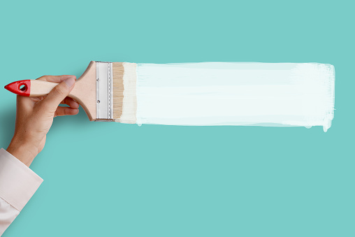 Man's hand holding paintbrush paint white color on blue aqua color wall, blank space for your text, banner, copyspace, advertising, or your design.