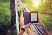 Beautiful girl is reading e-book in the hammock