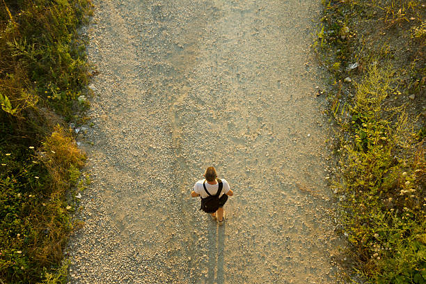 Man with backpack walking down the gravel road. Directly above view. Photo is taken with dslr camera and wide angle lens in sunset of summer day in European countryside.