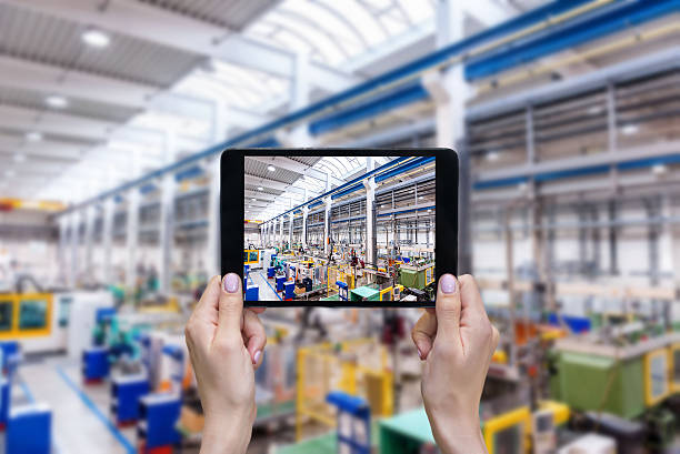 Futuristic factory & female hands holding tablet Horizontal color image of female hands holding a digital tablet in a modern plastic production line. Ordering on-line from injection moulding factory on a touchscreen tablet computer. Large factory, industrial machines, robots and manufacturing equipment arranged on clean and shiny flooring in background. digital transformation factory stock pictures, royalty-free photos & images