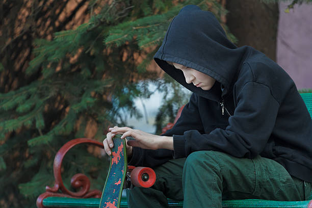 Retrato de un adolescente relajante mirando el monopatín en sus manos - foto de stock