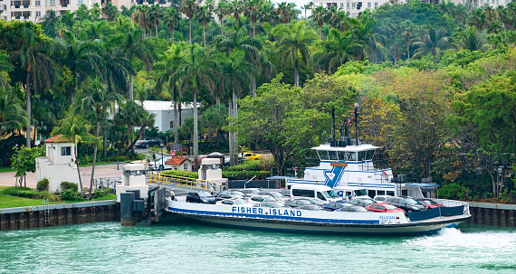 Fisher Island, United Stated - April 21, 2015: The Fisher Island Ferry arriving at the ferry dock on Fisher Island, Florida.  Fisher Island is located along Government Cut at the east end of the Bay of Biscayne, off the coast of Miami.  The ferry is the only way that cars can get from the mainland to the island.  Some of the island condominiums are visible behind the trees at the top of the image.  