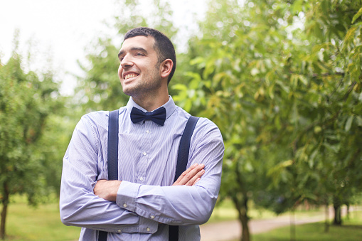 Smiling mid adult man posing with crossed arms, wearing shirt, suspenders and bow tie. About 30 years old, Caucasian male.