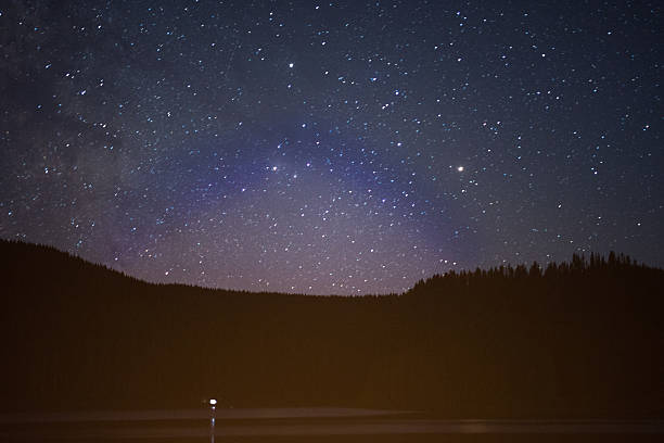 istock Starry night sky over mountain lake and forests 584589044