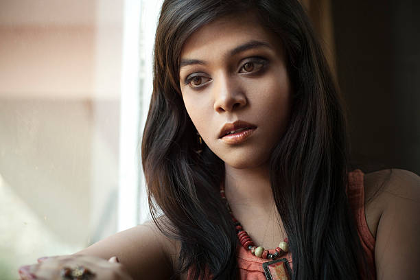 istock Serene girl looking away with blank expression sitting near window. 584590936