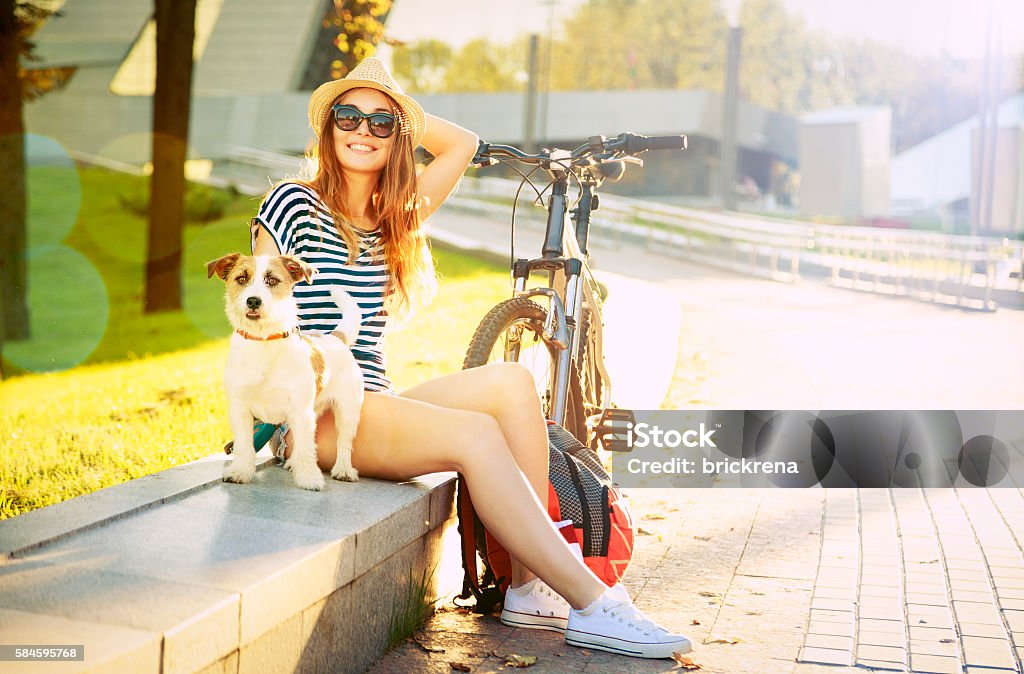 Smiling Hipster Girl with her Dog in Summer City Smiling Hipster Girl with her Dog and Bike in City. Happy Woman Enjoying Summer Lifestyle with Pet. Toned and Filtered Photo. Women Stock Photo