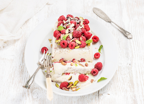 Homemade semifreddo with pistachio and raspberry in oval dish over old white painted wooden background, selective focus, horizontal composition