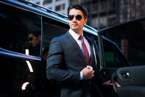 Handsome young businessman arriving in executive car wearing a suit and sunglasses in a city
