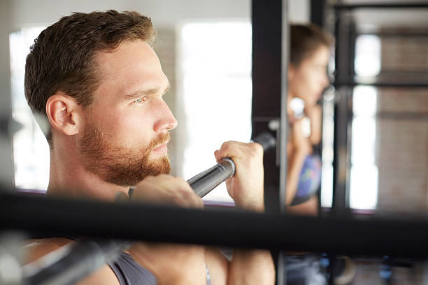 istock Determined man doing chin-ups with woman in gym 584612206