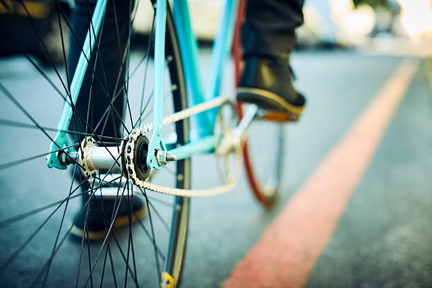Close-up of bicycle wheel with metal chain. Low section of man is riding cycle. Male is traveling on road.