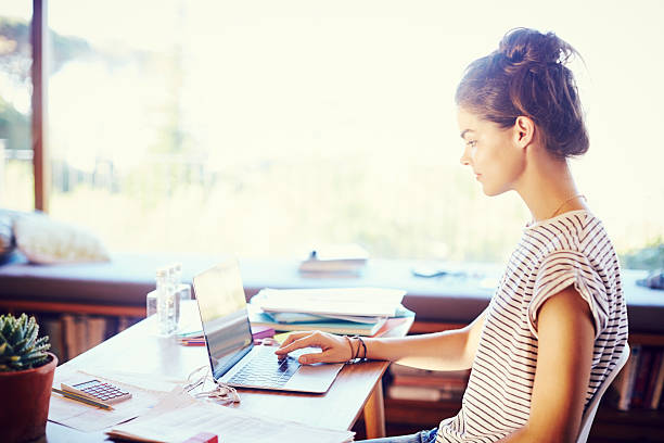 istock Side view of young female working on laptop at table 584746104