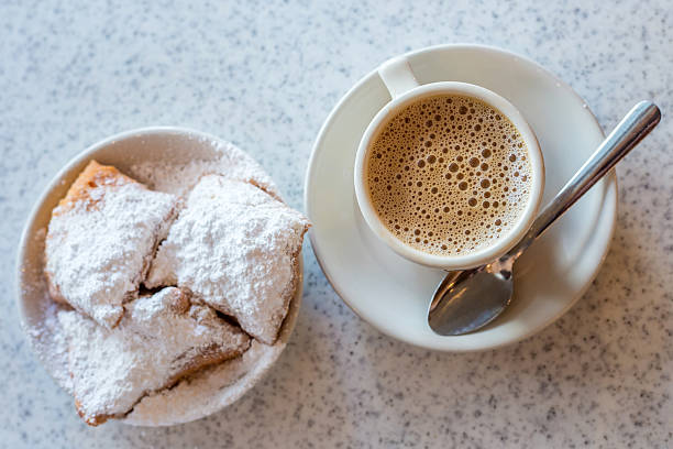 Beignets (French style donuts) Beignets (French style donuts) topped with sugar and a cup of coffee in the background new orleans stock pictures, royalty-free photos & images