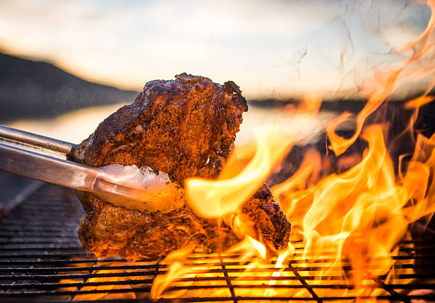 Steak Bbq A t-bone steak being char-grilled over open flames on an outdoors bbq.  serving tongs stock pictures, royalty-free photos & images