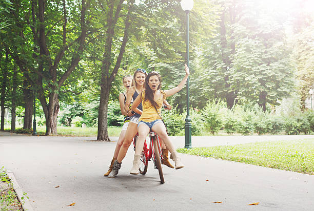 istock Happy boho chic girls ride together on bicycles in park 584751078