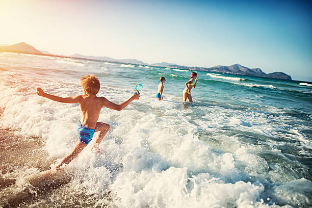 Summer vacations - kids playing at sea Three kids - a girl and two boys  - are having fun in sea.  Little boy is running and jumping in the sea, his brother and sister already standing in the sea. balearic islands stock pictures, royalty-free photos & images