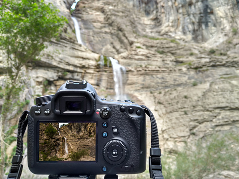 Close-up of digital camera making shot of beautiful waterfall