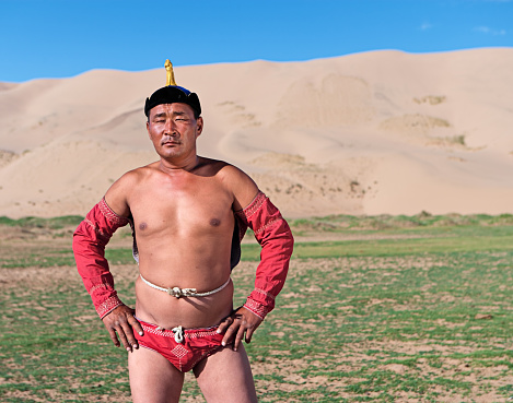 Mongolian wrestler posing during Naadam festival. He is standing on the grass, sand dunes on the background.http://bhphoto.pl/IS/mongolia_380.jpg