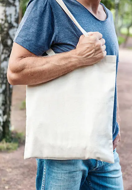 Man holding empty canvas bag outdoor. Template mock up