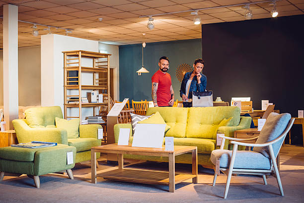 A middle aged couple are shopping in a furniture store for items for their new home. they are both browsing the living room items and look thoughtful.