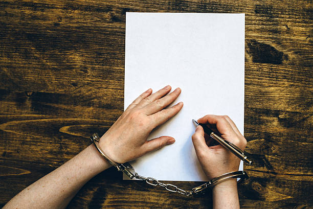 Female hands cuffed signing confession, top view Female hands cuffed signing confession, top view of police investigator detective desk interrogation woman stock pictures, royalty-free photos & images