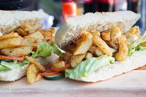 A close up of a couple of heart-stopping french fry sub sandwiches. (At least the lettuce is healthy right!) This type of sandwich is known by many different names world-wide, including Hoagie, Sub, Submarine, Footlong and Gatsby to name a few. 