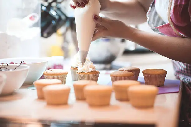 Woman making creamy top of cupcakes closeup. Selective focus.