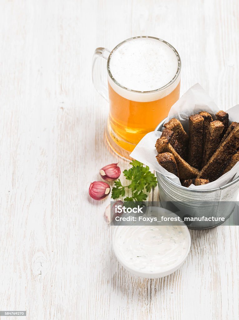 Beer snack set. Pint of pilsener in tall mug and Beer snack set. Pint of pilsener in tall mug and rye bread croutons with garlic cream cheese sauce over white painted old wooden background, top view, copy space, selective focus Alcohol - Drink Stock Photo