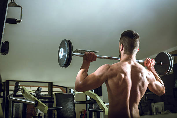 istock Young man lifting barbell. View from behind. 584770122