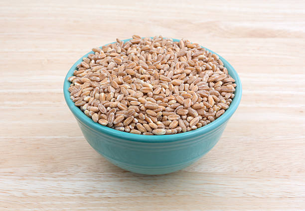 Side view of farrow organic grain filling a small bowl atop a wood table top.
