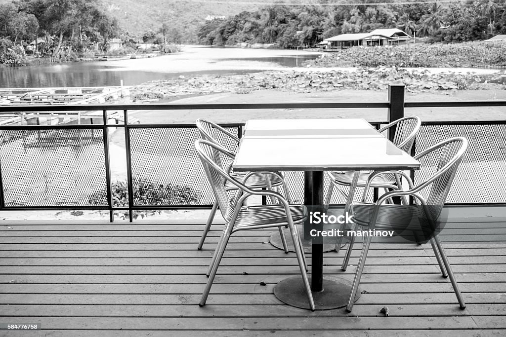 Outdoor furniture set in black and white Outdoor furniture including four stainless chairs and a stainless table on wooden floor. For leisure and having meal. Background is nature, water, river, mountain and forest. Black and white filter. Balcony Stock Photo