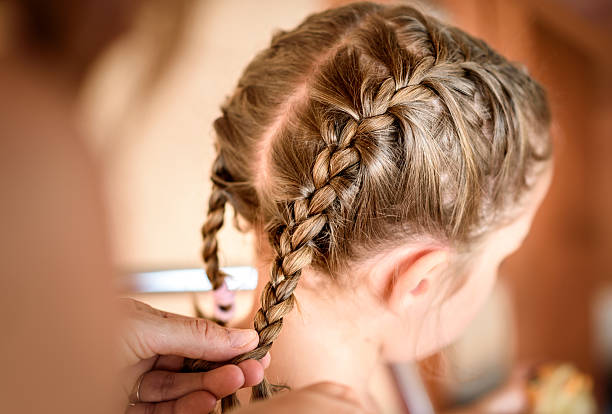 la madre está haciendo trenzas en la cabeza de la hija pequeña. - weaving fotografías e imágenes de stock