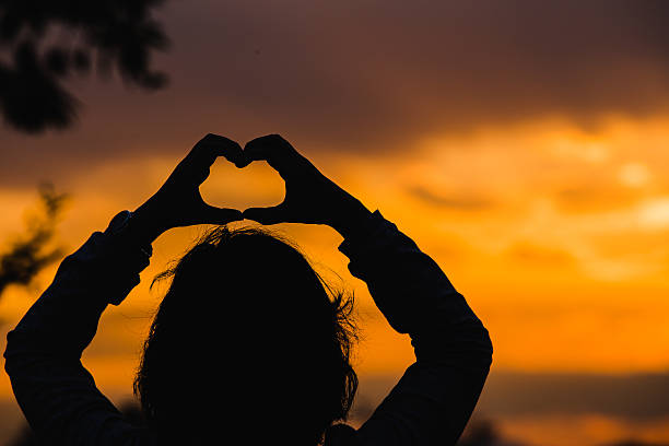 istock Women Silhouette with Hands in Heart Shape on Sunset Background 584778856