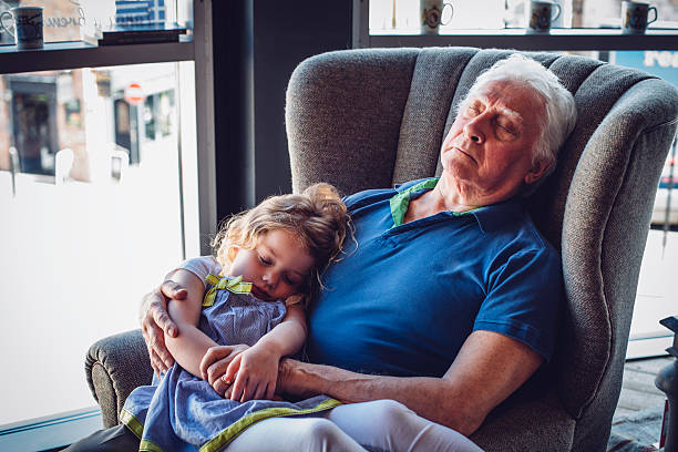Worn Out! Little girl asleep on her granddad's lap. He is holding her in his arms while asleep in an armchair. sleeping grandpa stock pictures, royalty-free photos & images