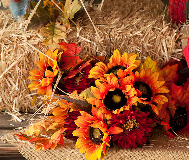 Dried floral arrangement in orange and brown hues.  The flowers lie on burlap with hay bale in background.