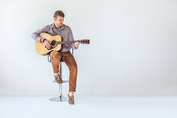 el apuesto guitarrista sonriente toca música en la silla - plucking an instrument fotografías e imágenes de stock