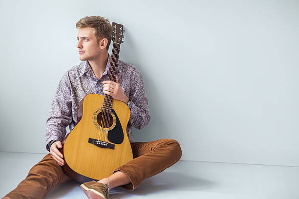 istock Portrait of handsome man with guitar siting on floor 584783882