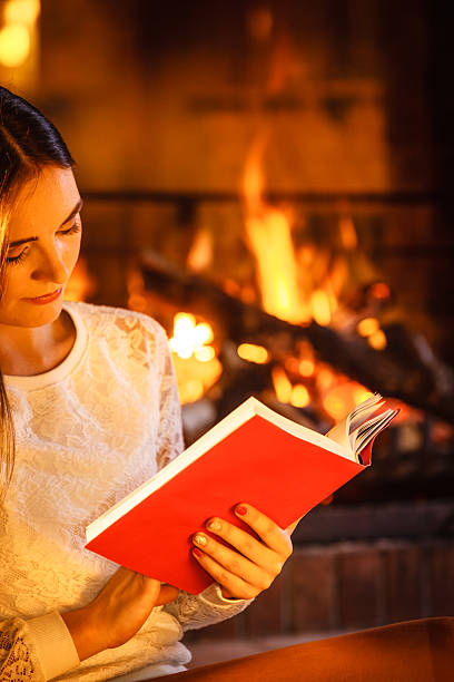 istock Woman reading book at fireplace. Winter home relax 584789278
